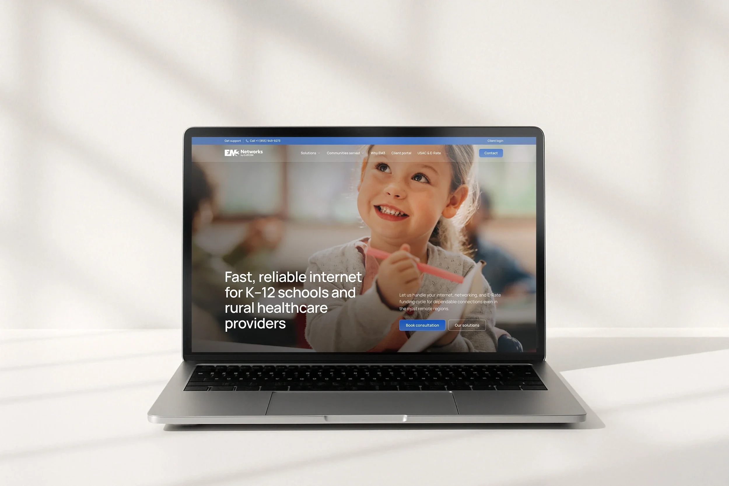 The EM3 Networks home page, 'Fast, reliable internet for K-12 schools and rural healthcare providers', on a laptop on a white desk